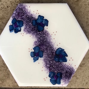 Abstract blue flowers on a purple and white background hand painted with alcohol inks on a ceramic hexagon tile coaster