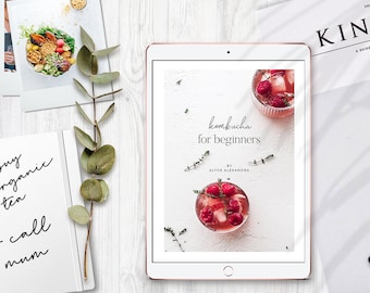 Puede incluir: Una tableta digital que muestra un fondo blanco con el texto "kombucha for beginners by Alyce Alexandra". El texto es negro y el fondo es blanco. Hay dos vasos de kombucha con frambuesas y tomillo en la pantalla. La tableta está sobre una superficie de madera blanca.
