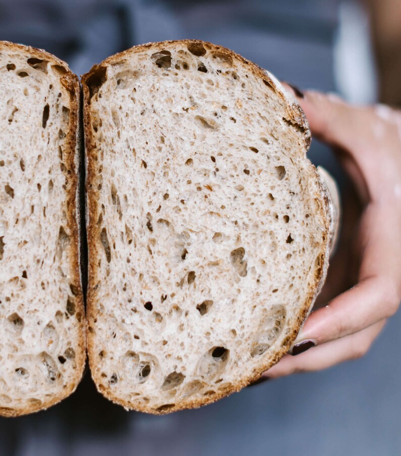 Peut inclure: Gros plan d'une miche de pain tranch&eacute;e, montrant la mie moelleuse et a&eacute;r&eacute;e et la cro&ucirc;te l&eacute;g&egrave;rement dor&eacute;e. Le pain est tenu dans une main, r&eacute;v&eacute;lant la texture et les d&eacute;tails du produit cuit.