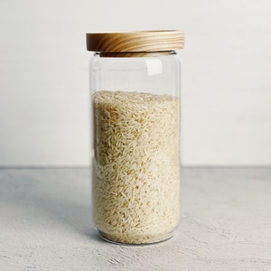 May include: A clear glass jar with a wooden lid filled with uncooked white rice.