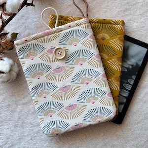 May include: Two fabric e-reader covers with a geometric pattern. One cover is white with gold and blue fans, and the other is mustard yellow with gold fans. The white cover has a button closure.