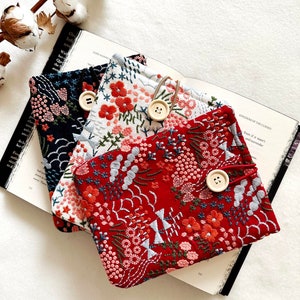 Puede incluir: Tres fundas de libro bordadas con motivos florales en rojo, blanco y azul. Las fundas tienen un cierre de botón y un lazo para un marcapáginas.