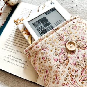 May include: A white e-reader with a floral patterned case. The e-reader is open to a book titled "Girl Missing". The case has a button on the front.