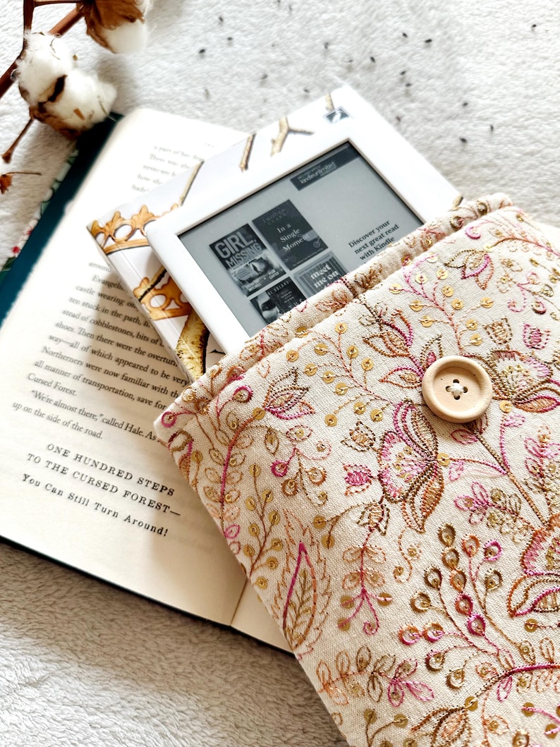 May include: A white e-reader with a floral patterned case. The e-reader is open to a book titled "Girl Missing". The case has a button on the front.