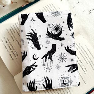 May include: White fabric book cover with a repeating pattern of black hands, moons, stars, and planets. The text "One Hundred Steps to the Cursed Forest - You Can Still Turn Around!" is printed on the cover.