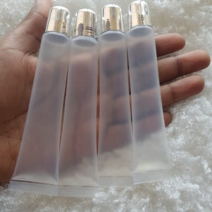 May include: Four clear plastic tubes with silver caps. The tubes are empty and are held in a hand.