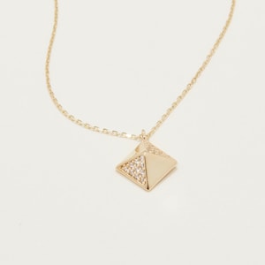 May include: A gold chain necklace with a small, gold, pyramid-shaped pendant that is encrusted with clear crystals.