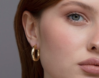 May include: A woman with long, red hair wearing gold hoop earrings and a gold chain necklace.