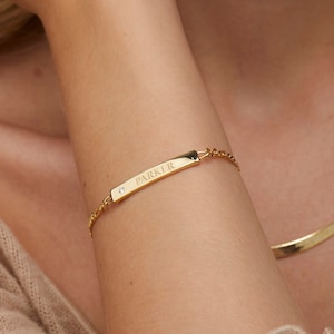 Puede incluir: Un brazalete de barra de oro con un pequeño diamante de acento y el nombre "PARKER" grabado en la barra.