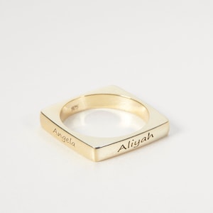 Puede incluir: Un anillo cuadrado de oro con los nombres "Angela" y "Aliyah" grabados en él.