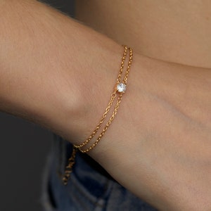 May include: A delicate gold chain bracelet with a single clear gemstone in the center.