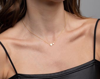 May include: A gold-toned necklace featuring a delicate chain and two small star-shaped charms of different sizes. The necklace rests against the collarbone, showcasing a polished metallic finish and a simple, refined design with a secure clasp.