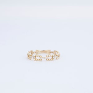 K&ouml;nnte beinhalten: Ein goldener Ring mit einem zarten Design aus kleinen runden Perlen und klaren Steinen.
