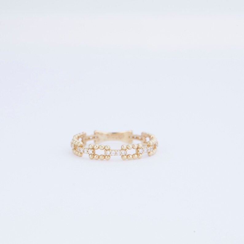 K&ouml;nnte beinhalten: Ein goldener Ring mit einem zarten Design aus kleinen runden Perlen und klaren Steinen.