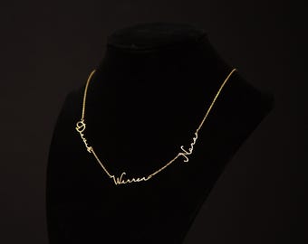 May include: A gold-toned necklace featuring three distinct names written in a cursive script font integrated directly into the chain. The names displayed are Denis, Warren, and Nara, connected by thin gold links in a delicate, minimalist design.