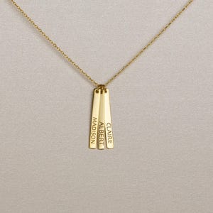 May include: A gold-toned necklace featuring a delicate chain and three vertical rectangular pendants. Each pendant is engraved with a name in a clean, sans-serif font, reading MADISON, ALBERT, and CLAIRE from left to right respectively.