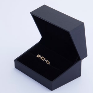 K&ouml;nnte beinhalten: Ein goldener Ring mit einem quadratischen Kettenmuster und kleinen Diamanten, die in das Metall gefasst sind. Der Ring wird in einer schwarzen Samt-Ringbox pr&auml;sentiert.