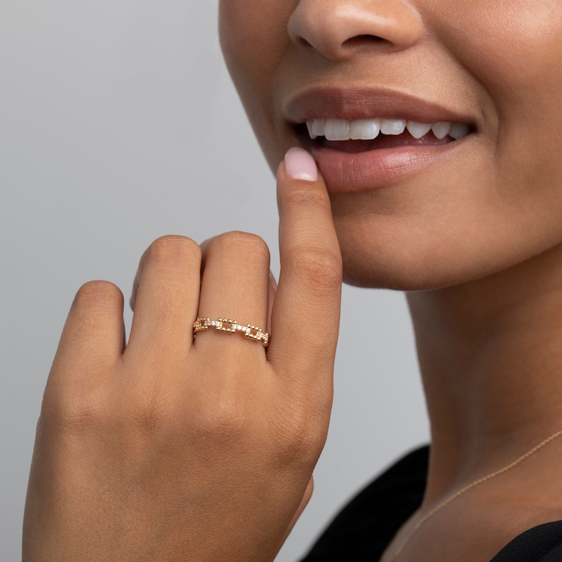 K&ouml;nnte beinhalten: Ein goldener Kettenring mit kleinen Diamanten, die in die Glieder eingefasst sind. Der Ring wird am Finger einer Person getragen.