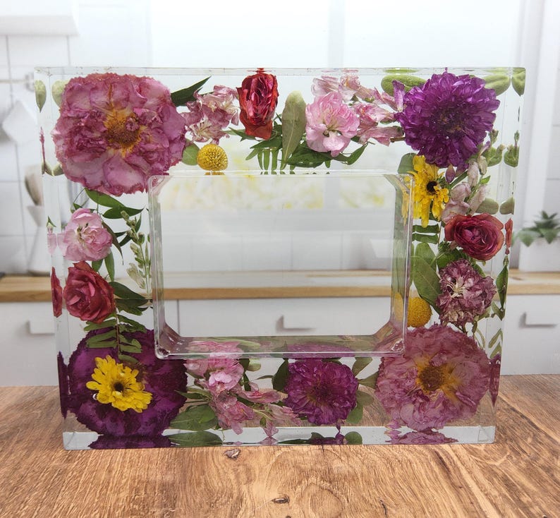 May include: A clear rectangular picture frame with a pressed flower design. The frame is filled with various dried flowers in shades of pink, purple, yellow, and red.