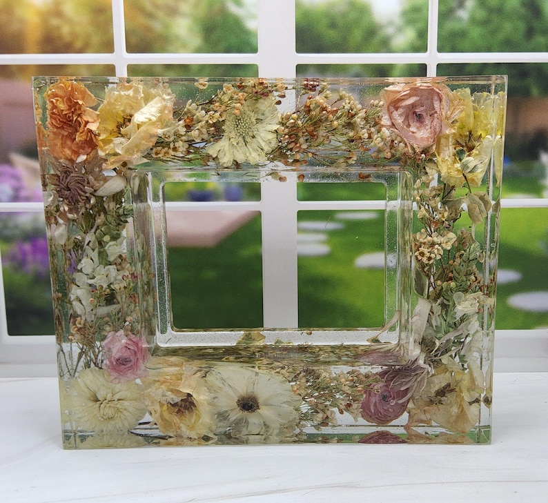 May include: A clear resin picture frame with pressed flowers and leaves in shades of pink, white, and yellow.