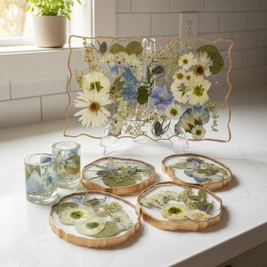 geode coasters, two shot glasses and geode tray with blue and white bouquet preservation inside on countertop near window.