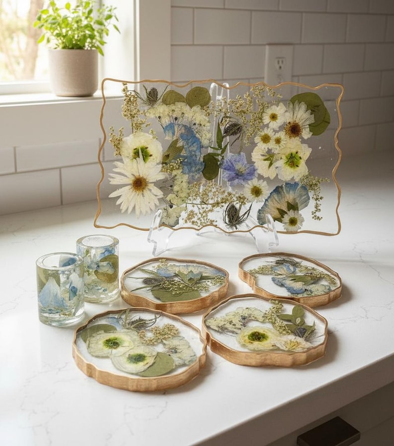 geode coasters, two shot glasses and geode tray with blue and white bouquet preservation inside on countertop near window.