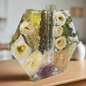 K&ouml;nnte beinhalten: Eine sechseckige, transparente Harzvase mit getrockneten Blumen und Gr&uuml;npflanzen im Inneren. Die Vase hat ein transparentes Rohr in der Mitte, um Wasser zu halten.