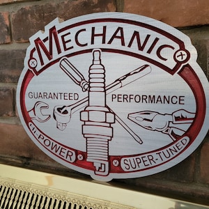 May include: Oval metal sign with the word "MECHANIC" in red lettering. The sign features a spark plug, wrench, pliers, and screwdriver. Text includes "GUARANTEED PERFORMANCE", "HI-POWER", and "SUPER-TUNED".