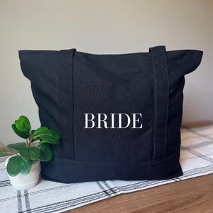 May include: Black canvas tote bag with the word "BRIDE" printed in white on the front.