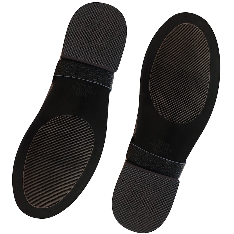 May include: The bottom of two black leather shoes with a textured sole. The shoes have a black leather strap with the text "Allbirds - Wool Runners" printed on them.