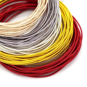 Op de afbeelding: Een close-up van een stapel kleurrijke, metalen, gewikkelde draad. De draad is gerangschikt in een regenboogpatroon, beginnend met rood, dan geel, zilver en ten slotte beige.