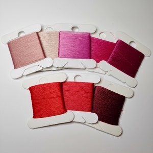 Puede incluir: Una colección de carretes de hilo de bordar coloridos en tonos rosa, rojo y burdeos. Los carretes están dispuestos sobre tarjetas de cartón blanco, mostrando una gama de tonos desde el rosa claro hasta el carmesí intenso. Ideal para varios proyectos de manualidades.
