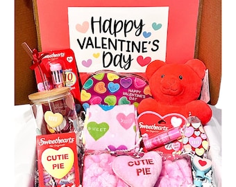 May include: A pink and red Valentine's Day gift box filled with various items, including a plush red teddy bear, a pink heart-shaped pillow, a pink and white striped towel, a glass jar with candy hearts, a box of Sweethearts candies, a pink lip balm, and a pink and white heart-shaped candy dish. The box is decorated with a sign that says "Happy Valentine's Day".