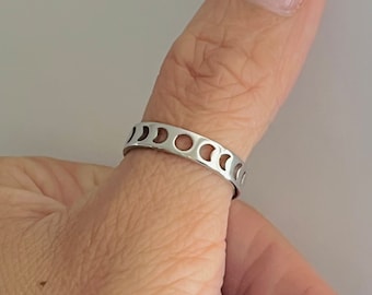 May include: A silver ring with a moon phase design. The ring is worn on a person's thumb.