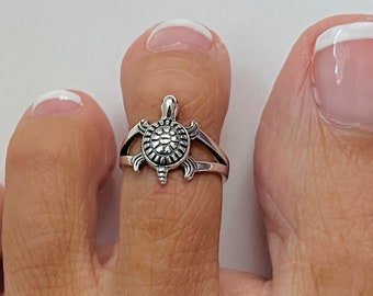 Könnte beinhalten: Silberner Zehenring mit einem Schildkrötenmotiv. Der Ring ist offen und verstellbar, um den meisten Zehengrößen zu passen.
