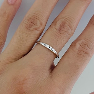 May include: A silver ring with a cross and wings design. The ring is on a person's finger.