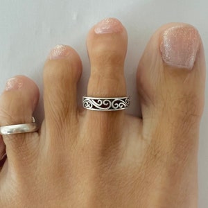 Puede incluir: Un anillo de dedo del pie de plata con un diseño delicado y en espiral. El anillo se lleva en el segundo dedo del pie.
