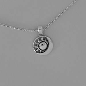 May include: A silver necklace with a pendant featuring a sun and moon design. The pendant is round and has a detailed sun with rays and a crescent moon.
