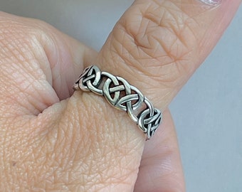 May include: A silver Celtic knot ring with a detailed design. The ring is worn on a person's thumb.