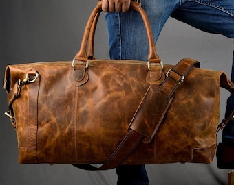 May include: A brown leather duffel bag with a long strap and two handles. The bag is worn and has a distressed look.