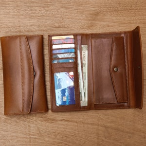 May include: A brown leather wallet with multiple card slots and a billfold. The wallet is open and has several cards and bills inside.