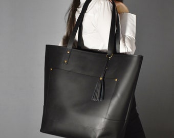 May include: A black leather tote bag with a gold tassel and a front pocket. The bag has a top zipper closure and two handles.