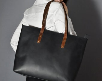 May include: A black leather tote bag with brown leather straps and gold accents. The bag has a spacious interior and is perfect for carrying everyday essentials.