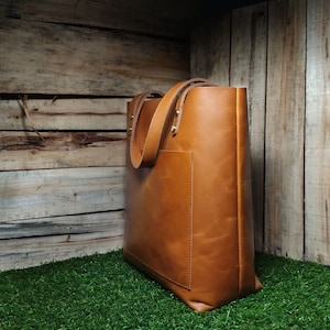May include: A brown leather tote bag with a front pocket. The bag has a top zipper closure and two handles.