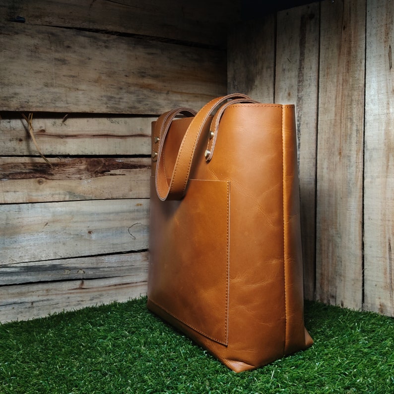 May include: A brown leather tote bag with a front pocket. The bag has a top zipper closure and two handles.