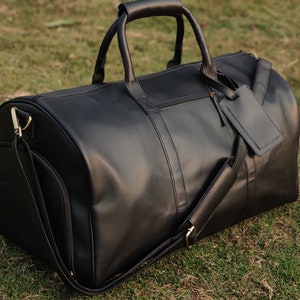 May include: A black leather duffel bag with a top handle and a shoulder strap. The bag has a zippered closure and a small leather tag attached to the zipper.
