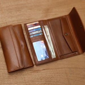 May include: A brown leather wallet with multiple card slots and a billfold. The wallet is open to reveal several cards and cash.