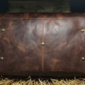 May include: A brown leather duffel bag with brass accents. The bag has a textured surface and a zipper closure.