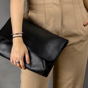 May include: A black leather clutch bag with a fold-over flap.