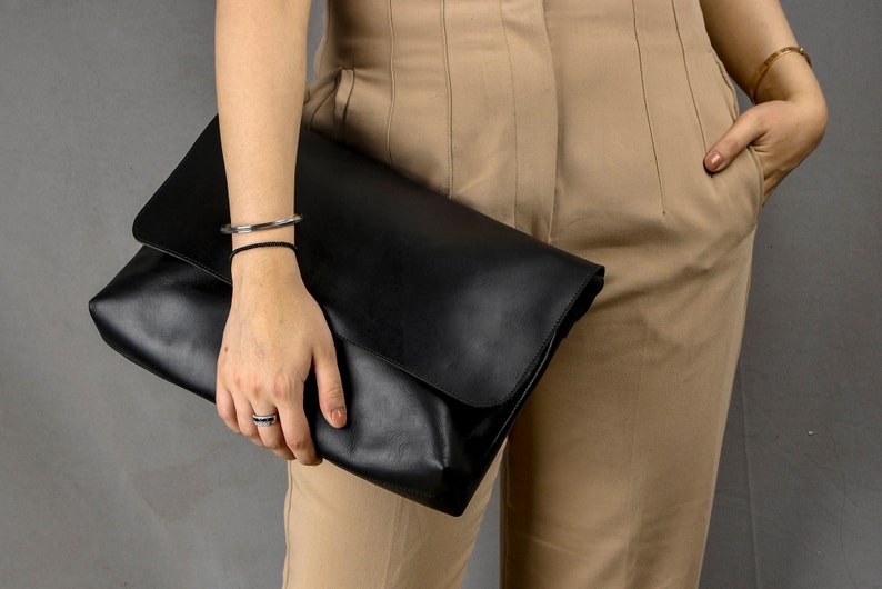May include: A black leather clutch bag with a fold-over flap.